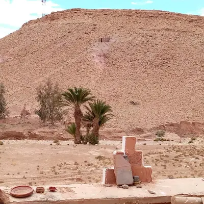 a hill with palm trees and a building in the desert at Dar adiafa dar asalam in Aït Ben Haddou