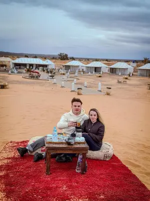a man and woman sitting on a table on the beach at Merzouga Night Camp in Merzouga