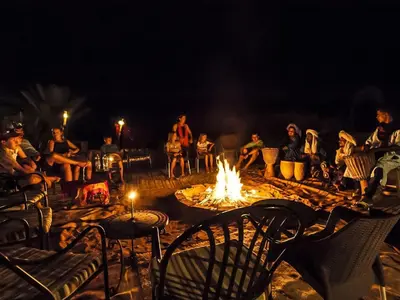 a group of people sitting around a fire at night at Merzouga Night Camp in Merzouga