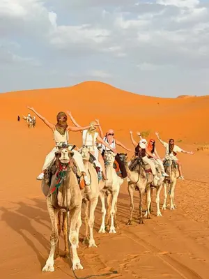 a group of people riding on camels in the desert at Merzouga Night Camp in Merzouga