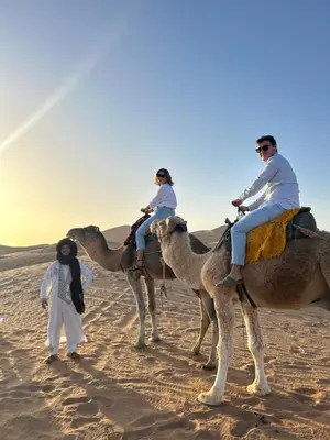three people are riding on camels in the desert at Camp Sakura Desert Dream in Merzouga