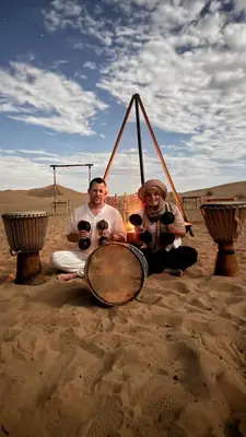 two people sitting in the desert holding wine glasses at Camp Sakura Desert Dream in Merzouga