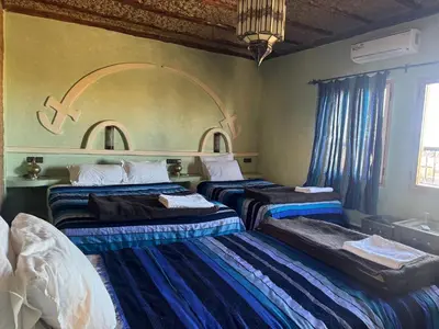 a hotel room with three beds and a window at Riad Ksar Merzouga in Merzouga