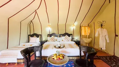 a bedroom with two beds and a table and chairs at Merzouga Alicante Luxury Camp in Merzouga
