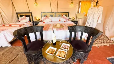 a bedroom with two beds and a table and chairs at Merzouga Alicante Luxury Camp in Merzouga