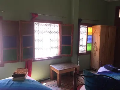 a room with two beds and windows and a table at Riad Selma in Meknès