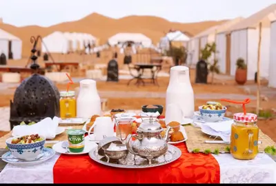 a table with a red table cloth with food on it at Aisha Luxury Camp in Merzouga