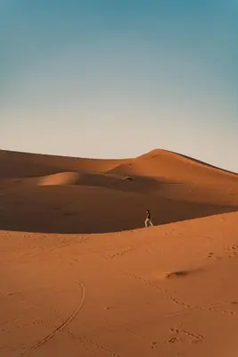 a person walking on a sand dune in the desert at Aisha Luxury Camp in Merzouga