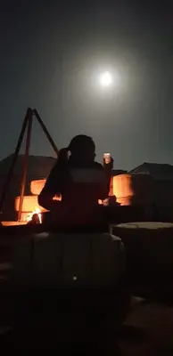 a person sitting on a ledge at night with a drink at Aisha Luxury Camp in Merzouga