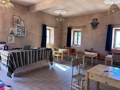 a room with a bed and tables and chairs at Auberge Camping La Libertè in Merzouga