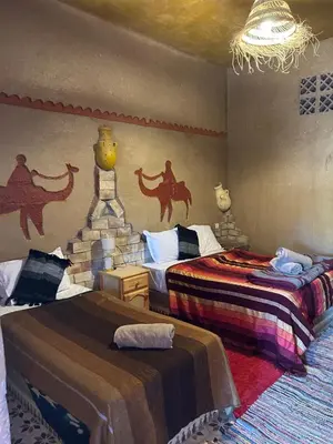 a bedroom with two beds and a wall with camel paintings at Auberge Camping La Libertè in Merzouga