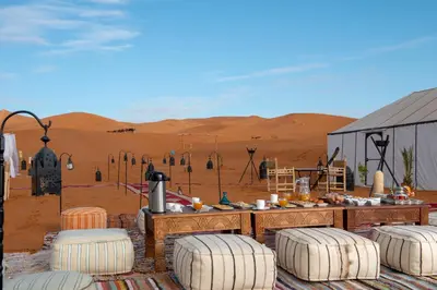 a desert outpost with a table and chairs in the desert at Alibaba Merzouga Camp in Merzouga