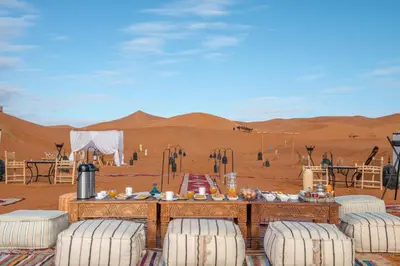a table in the middle of a desert with chairs at Alibaba Merzouga Camp in Merzouga