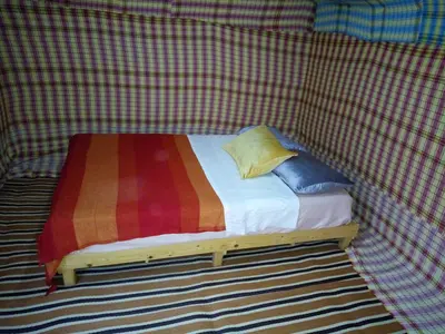 a small bed in a tent with a colorful blanket at Sahara camel tours camp in Merzouga