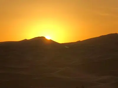 a sunset over a mountain with the sun setting behind it at Sahara camel tours camp in Merzouga
