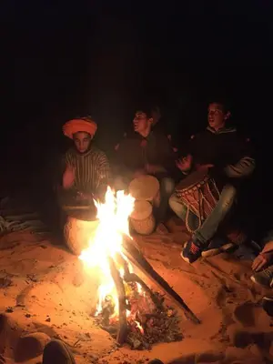 a group of people sitting around a fire at Sahara camel tours camp in Merzouga
