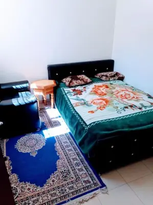a bedroom with a bed and a table and a rug at Cozzy F2 appartement Ifrane in Ifrane