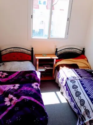 a bedroom with two beds and a table and a window at Cozzy F2 appartement Ifrane in Ifrane