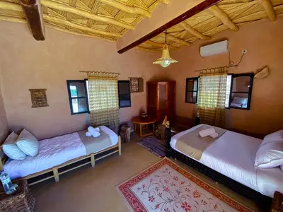 a room with two beds and a table and windows at Maison d'hôtes imouzzar asfalou in Aït Ben Haddou