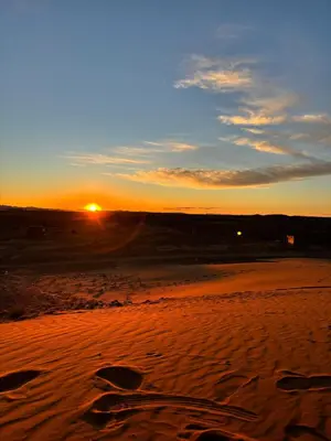 a sunset on a beach with the sun in the distance at Camp Desert Sky in Merzouga