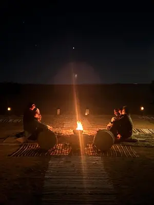 a group of people sitting around a fire at night at Camp Desert Sky in Merzouga