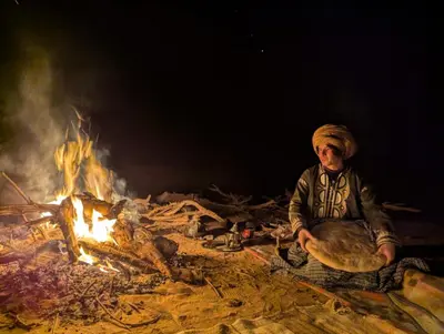 a man sitting in front of a fire at Camp Local Family in Mhamid