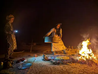 two women standing around a fire with a pot of food at Camp Local Family in Mhamid