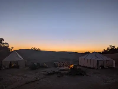 a group of tents in a field with the sunset at Camp Local Family in Mhamid