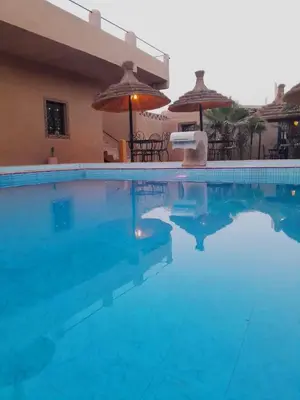 a swimming pool with blue water and umbrellas at Merzouga Riad Desert Man in Merzouga
