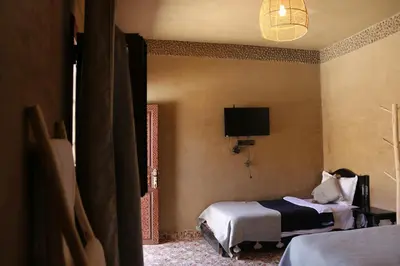 a bedroom with two beds and a tv on the wall at Merzouga Riad Desert Man in Merzouga