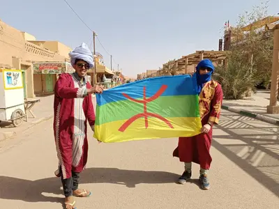 two people are holding a flag on a street at Guest House Nomad Life in Merzouga