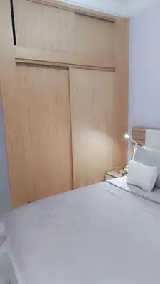 a bedroom with a white bed with a wooden door at Appartement Basatine in Fès