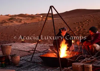two men sitting around a fire in the desert at Merzouga Desert Camps in Merzouga