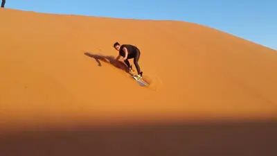 a man riding a surfboard on a sand dune at Riad camels house in Merzouga