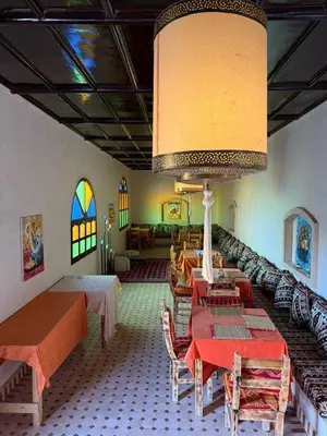 a dining room with tables and chairs and a large chandelier at Riad camels house in Merzouga