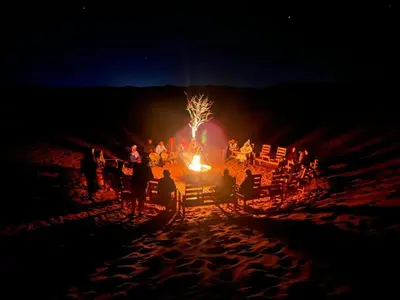 a group of people sitting around a bonfire on a beach at night at Idir Luxury Camp in Merzouga
