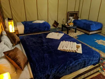 a room with two beds and a table in a tent at Royal Sands Luxury Camp in Merzouga