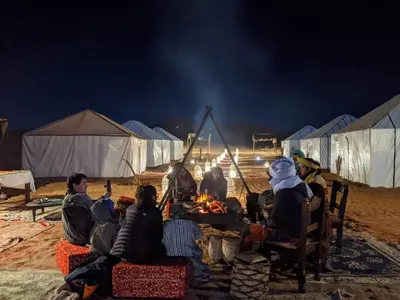 a group of people sitting around a fire at night at Royal Sands Luxury Camp in Merzouga