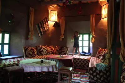 a woman standing in a living room with a couch at Kasbah Maison D’hôte Lalla Zahra in Aït Baha