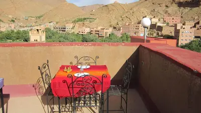 a red table and chairs on a balcony with a city at Kasbah Maison D’hôte Lalla Zahra in Aït Baha