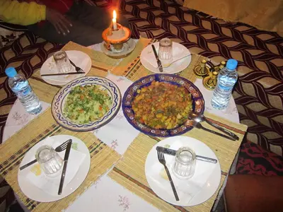 a table with plates of food on a table with a candle at Kasbah Maison D’hôte Lalla Zahra in Aït Baha