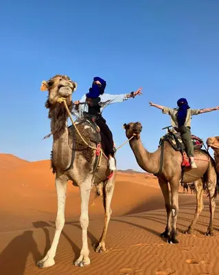 three people riding on the backs of camels in the desert at Merzouga Exclusive Camp in Merzouga
