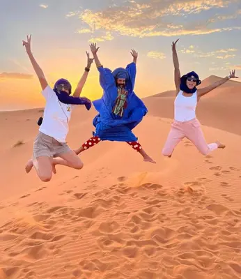 three people jumping in the sand in the desert at Merzouga Exclusive Camp in Merzouga