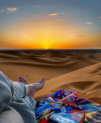 a person laying in the desert watching the sunset at Riad Dar Maria in Merzouga