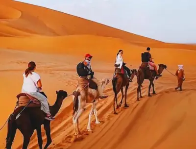 a group of people riding camels in the desert at Riad Dar Maria in Merzouga