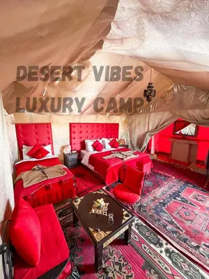 a room with two beds and red furniture in a tent at Desert vibes Luxury camp in Merzouga