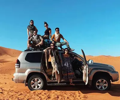 a group of people sitting on the roof of a car in the desert at Merzouga Berber Camp in Merzouga