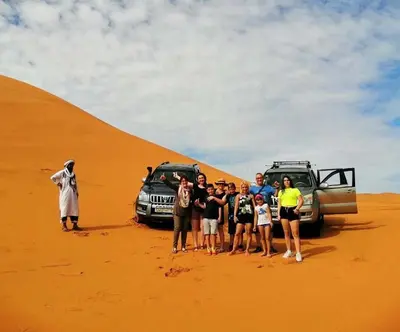 a group of people standing in front of a sand dune at Merzouga Berber Camp in Merzouga