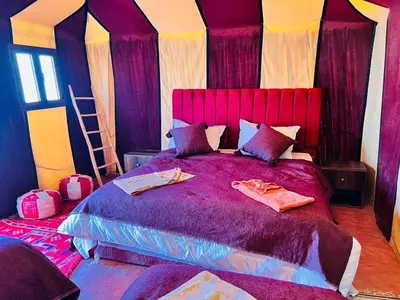 a bedroom with a large purple bed with pillows at Merzouga Berber Camp in Merzouga