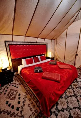 a bedroom with a red bed in a tent at Majestic Dunes Luxury Camp in Merzouga